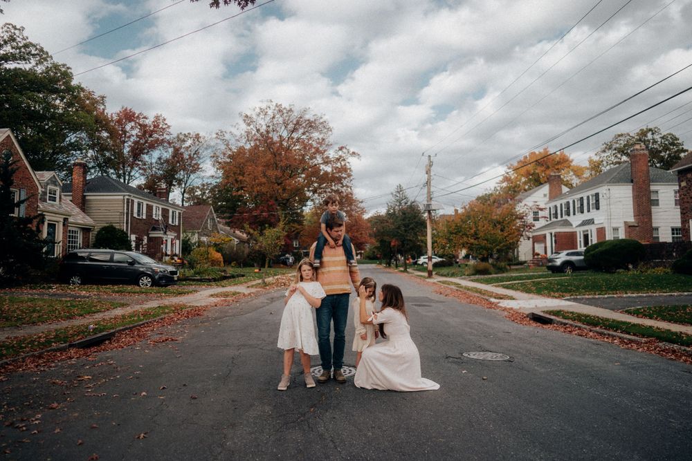 A family walks together on a leaf-covered suburban street during fall season.