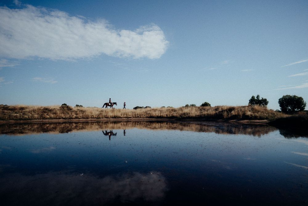 A serene landscape with a horse rider silhouetted against a reflective lake and blue sky.