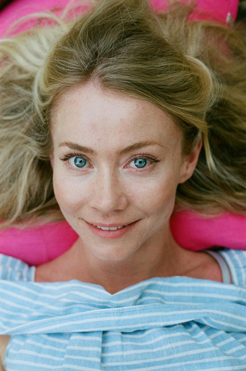 A close-up portrait against pink background showing bright blue eyes and blonde hair.