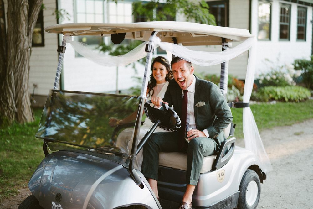 A couple sits in a white golf cart decorated for a wedding celebration at an outdoor venue.