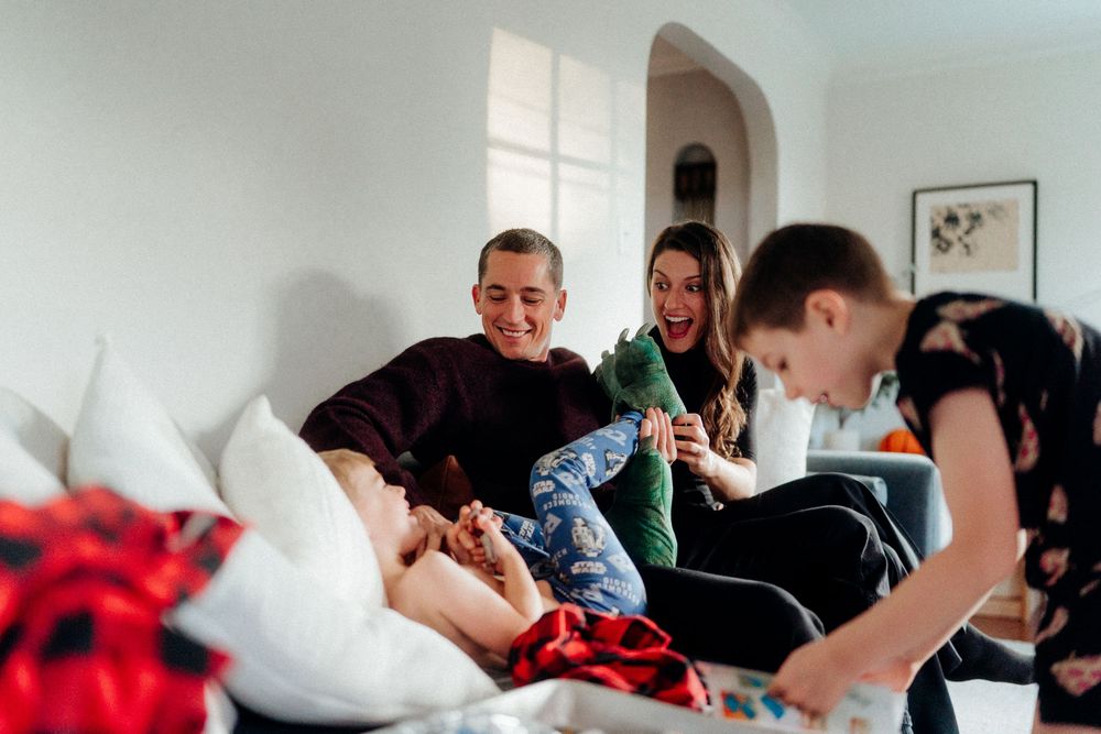 Family laughing together on a couch during Christmas, with wrapped gifts in the foreground.