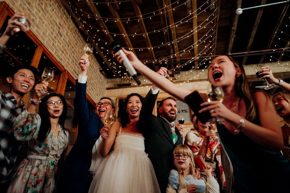 Joyful bride and groom celebrate with guests raising champagne glasses at their wedding reception.