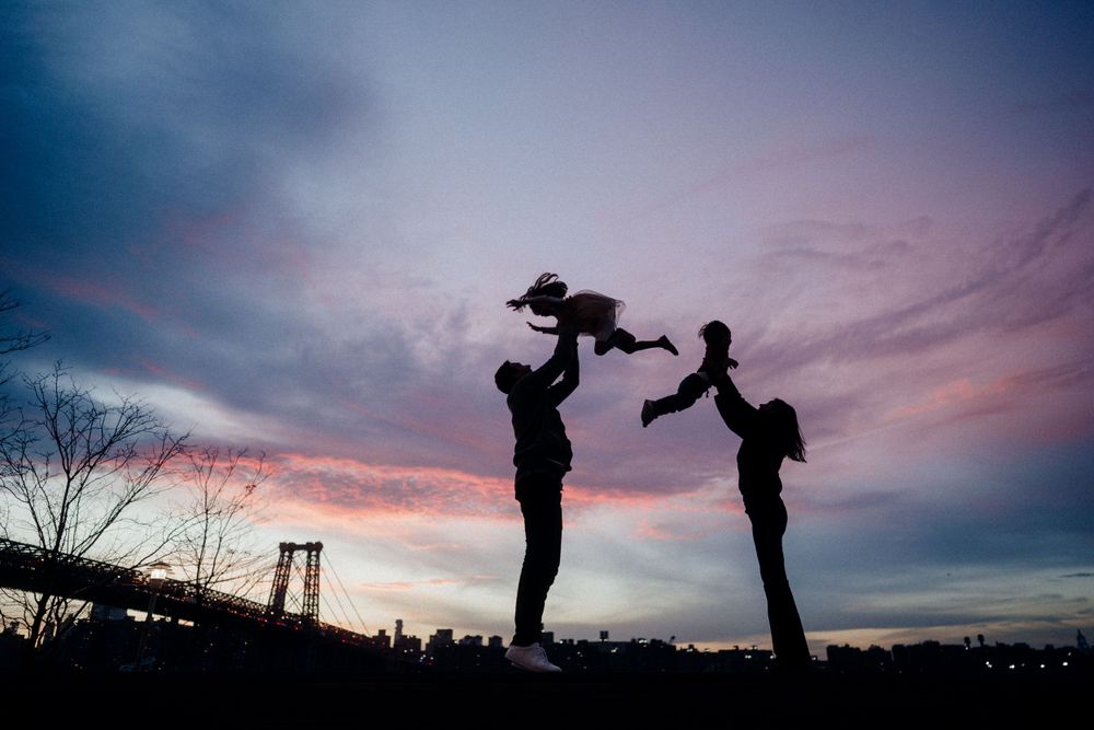 Silhouettes of parents playing with child against a dramatic purple sunset sky.