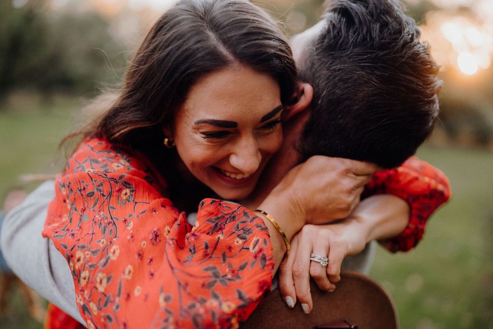Joyful embrace captured during sunset with person wearing bright coral sweater.