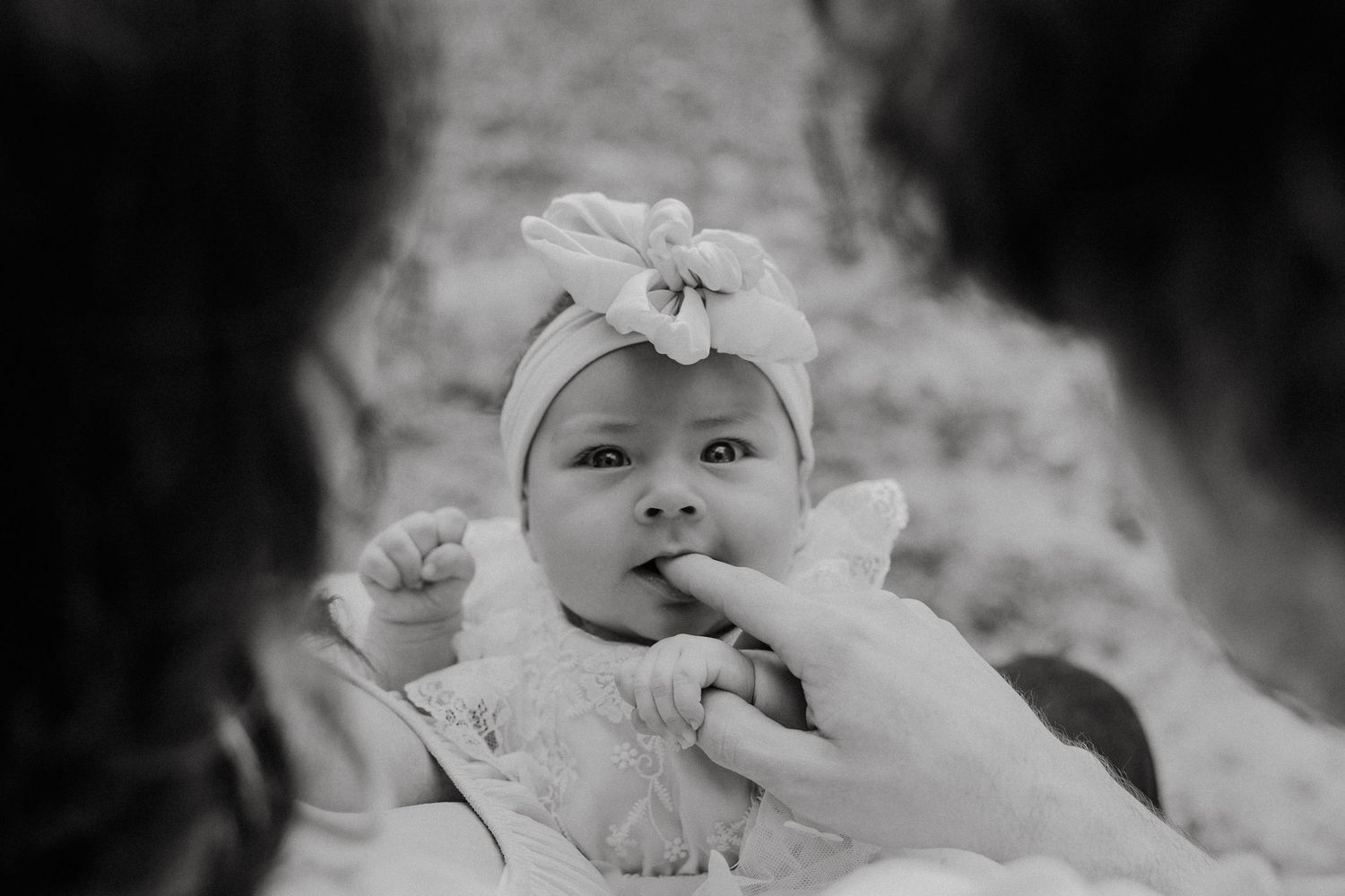 Baby wearing white lace dress and floral headband in black and white portrait.