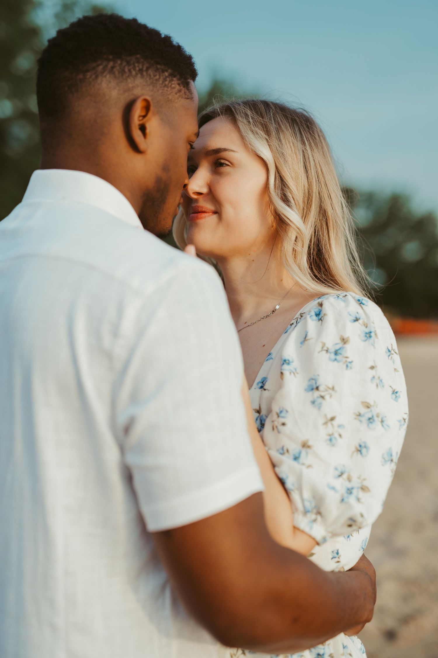 Couple sharing a romantic moment outdoors near Milwaukee Lakefront. Woman in floral dress smiling at man in white shirt. Southeast Wisconsin