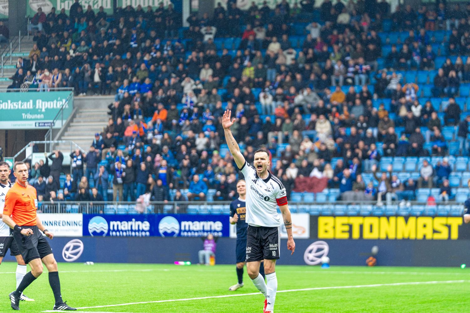 Soccer player waves to crowd in a packed stadium during a professional football match on a cloudy day.