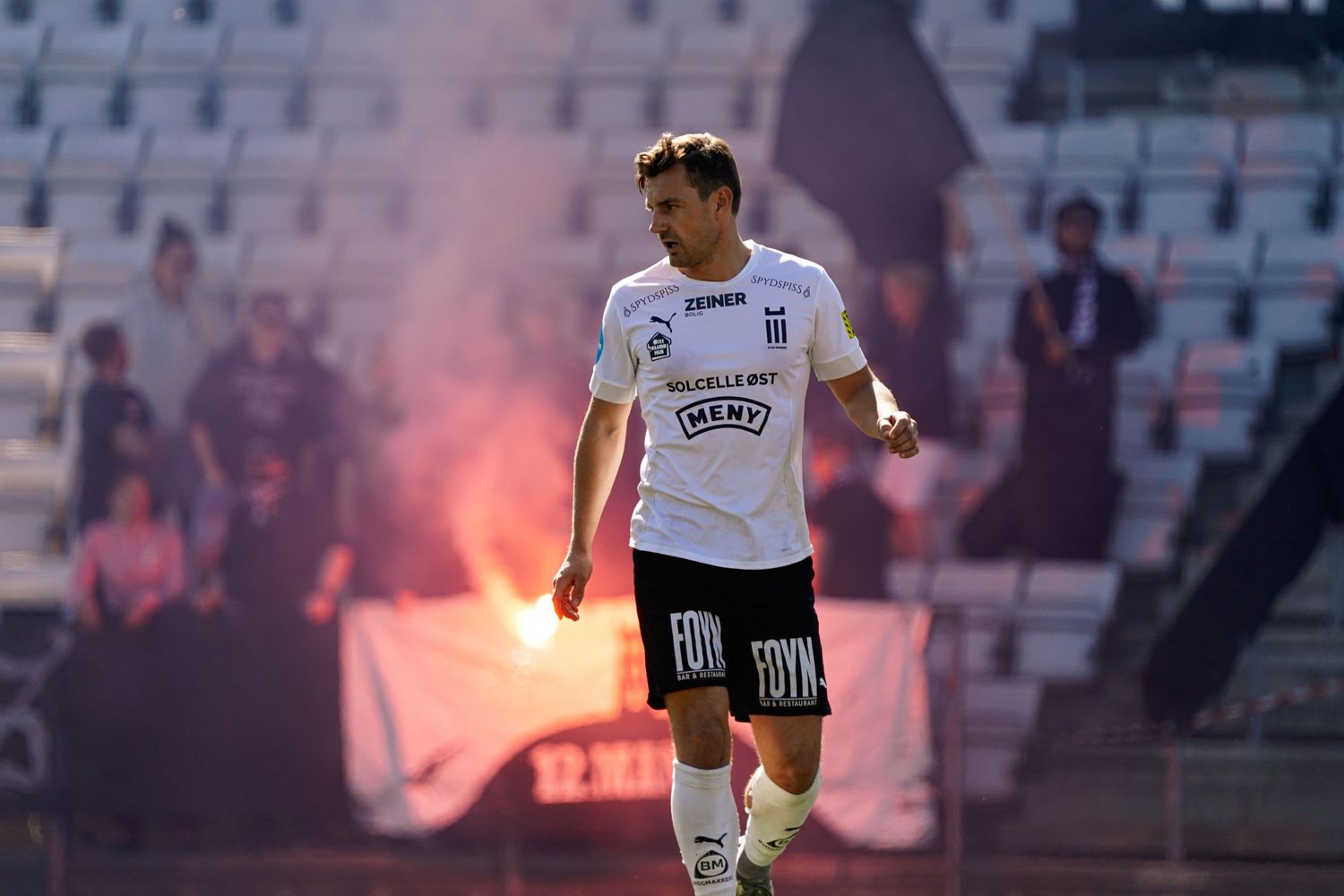 Fotballspiller foran bluss på tribunen