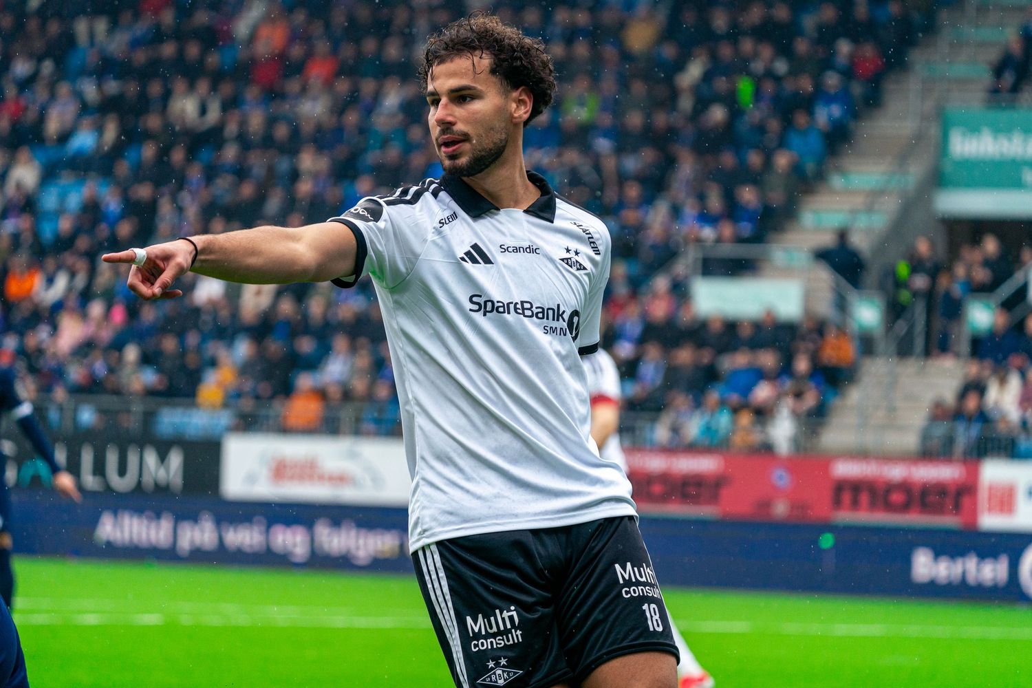 Football player in black and white Rosenvik kit pointing during a match at a packed stadium.