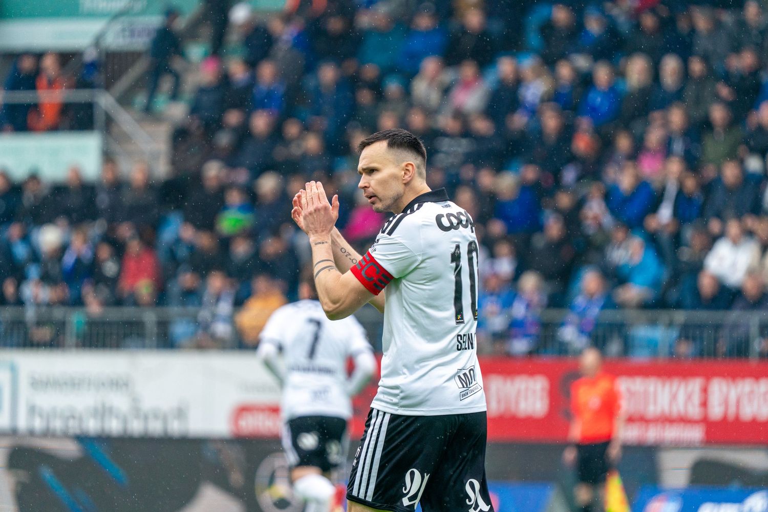 Soccer player in black and white jersey applauding fans during a match at a crowded stadium.