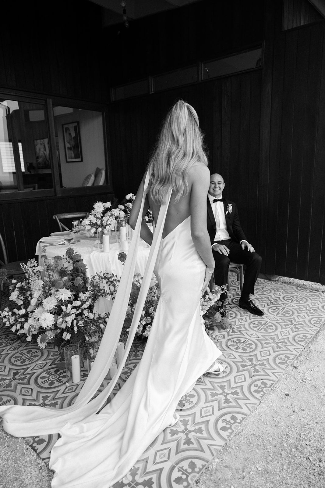 Bride in flowing white gown with long veil stands in rustic wood-paneled room.