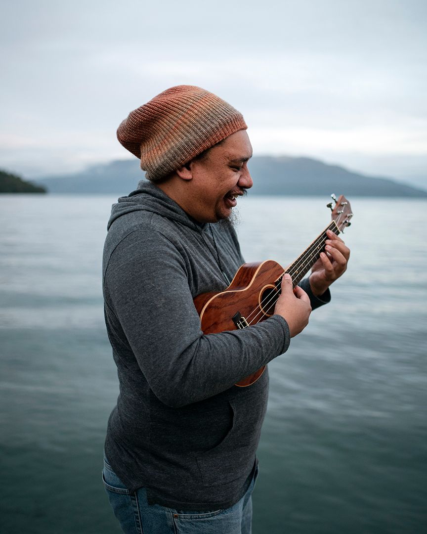 Portrait of a Maori Man playing a ukelele, a mountain and lake in the background