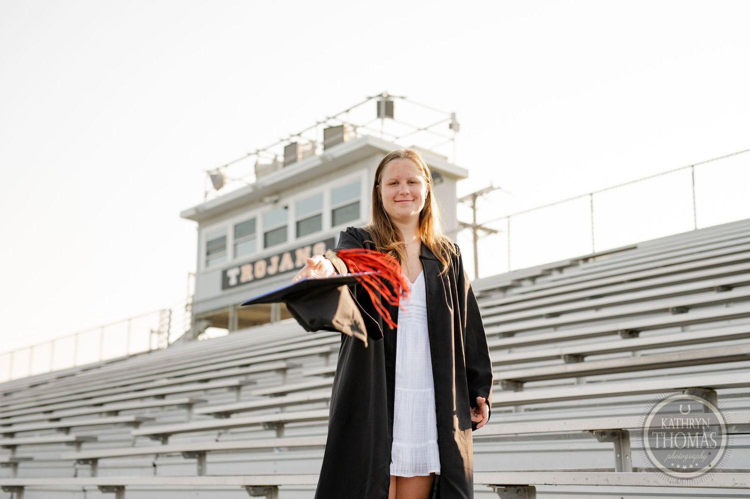 Graduate holds diploma while posing on stadium bleachers during golden hour.