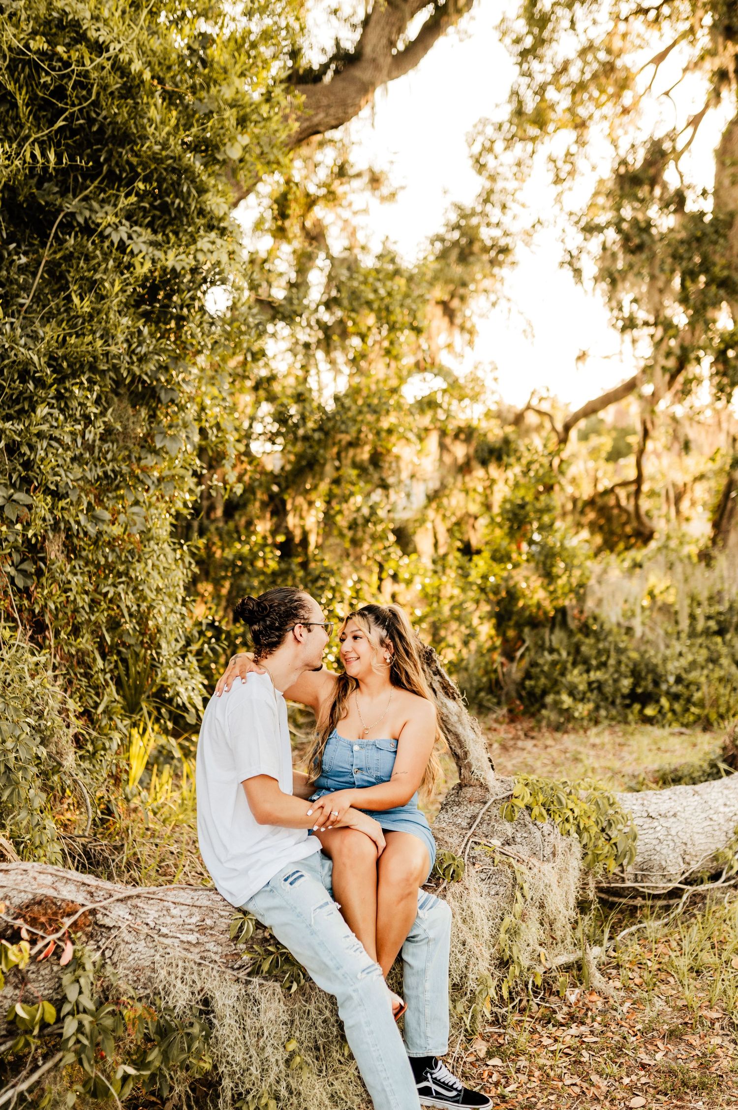 A romantic couple shares an intimate moment while sitting on a log in a golden-lit forest.