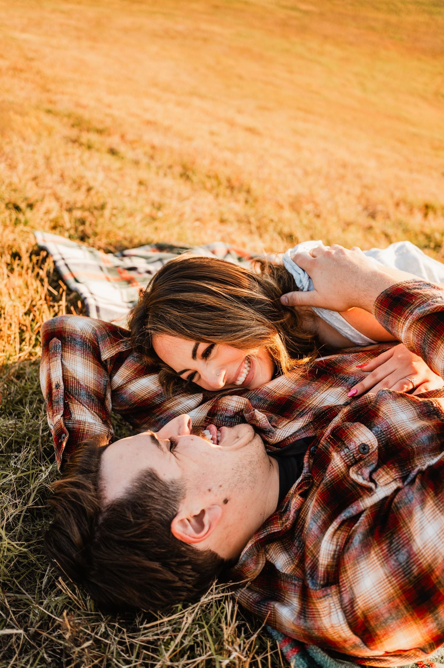 Playful couple relaxing in sun-drenched field wearing plaid shirt and casual attire.