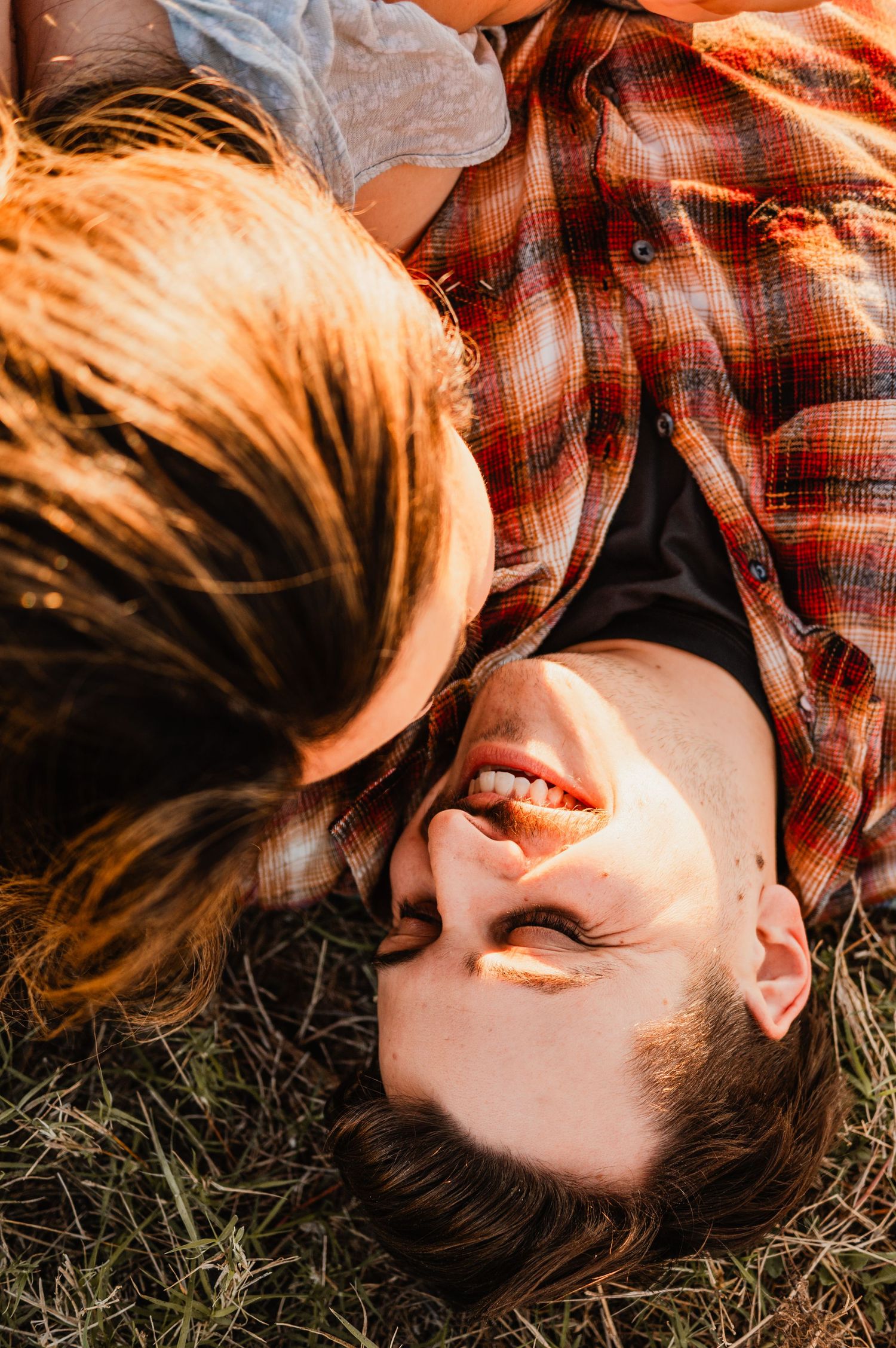 Person lying in grass wearing plaid shirt captured in warm sunlit tones during golden hour.