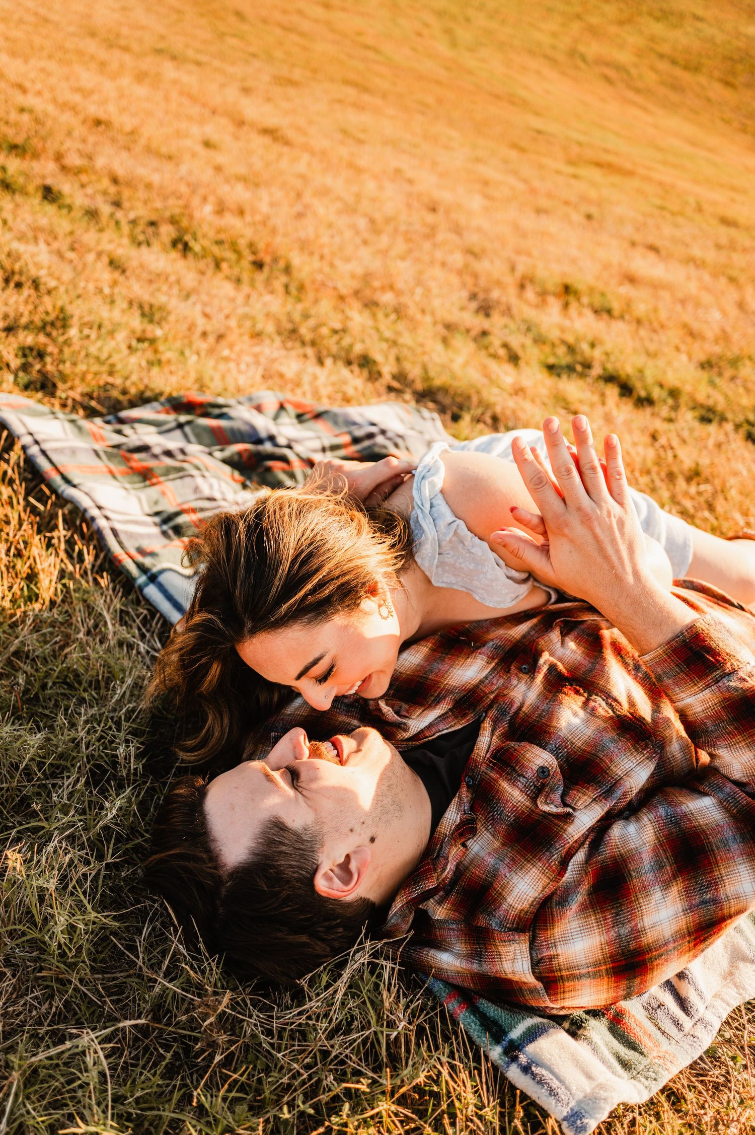 Couple sharing an intimate moment while lying in a sun-drenched autumn field with warm golden tones.