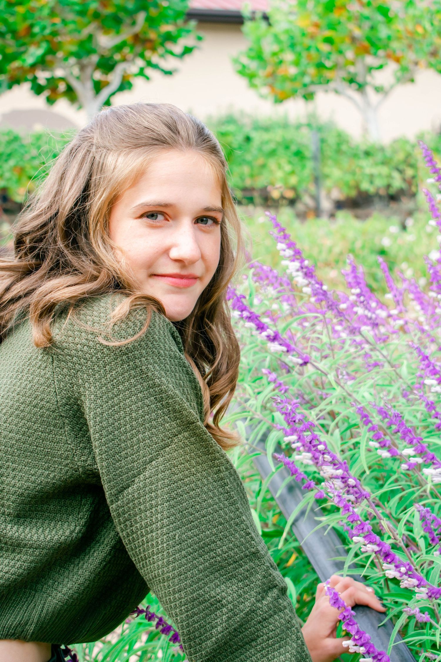 Green knit sweater photographed among purple wildflowers in garden setting.