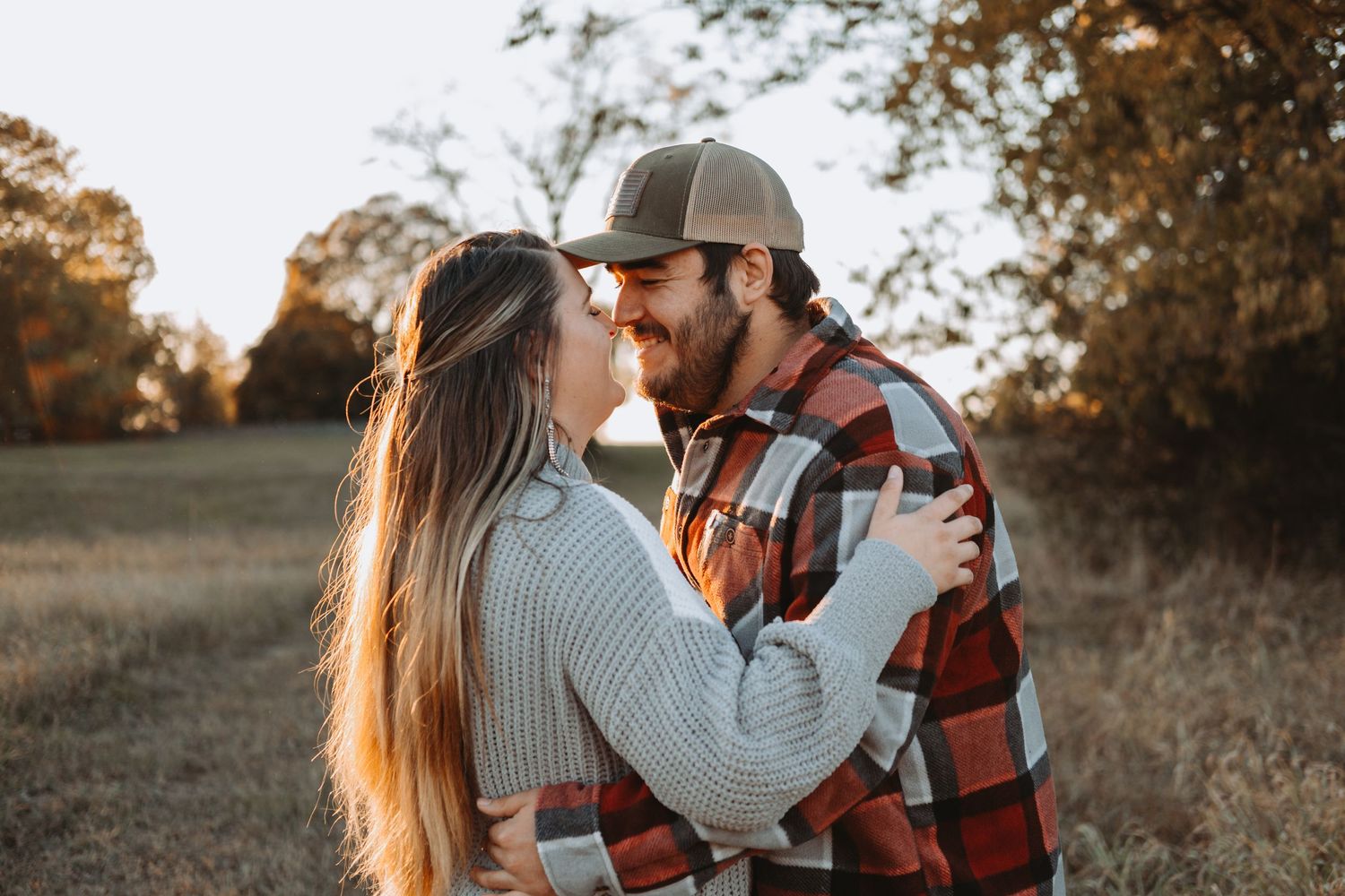 A romantic couple embraces in a field during golden hour sunset as they share an intimate autumn moment.