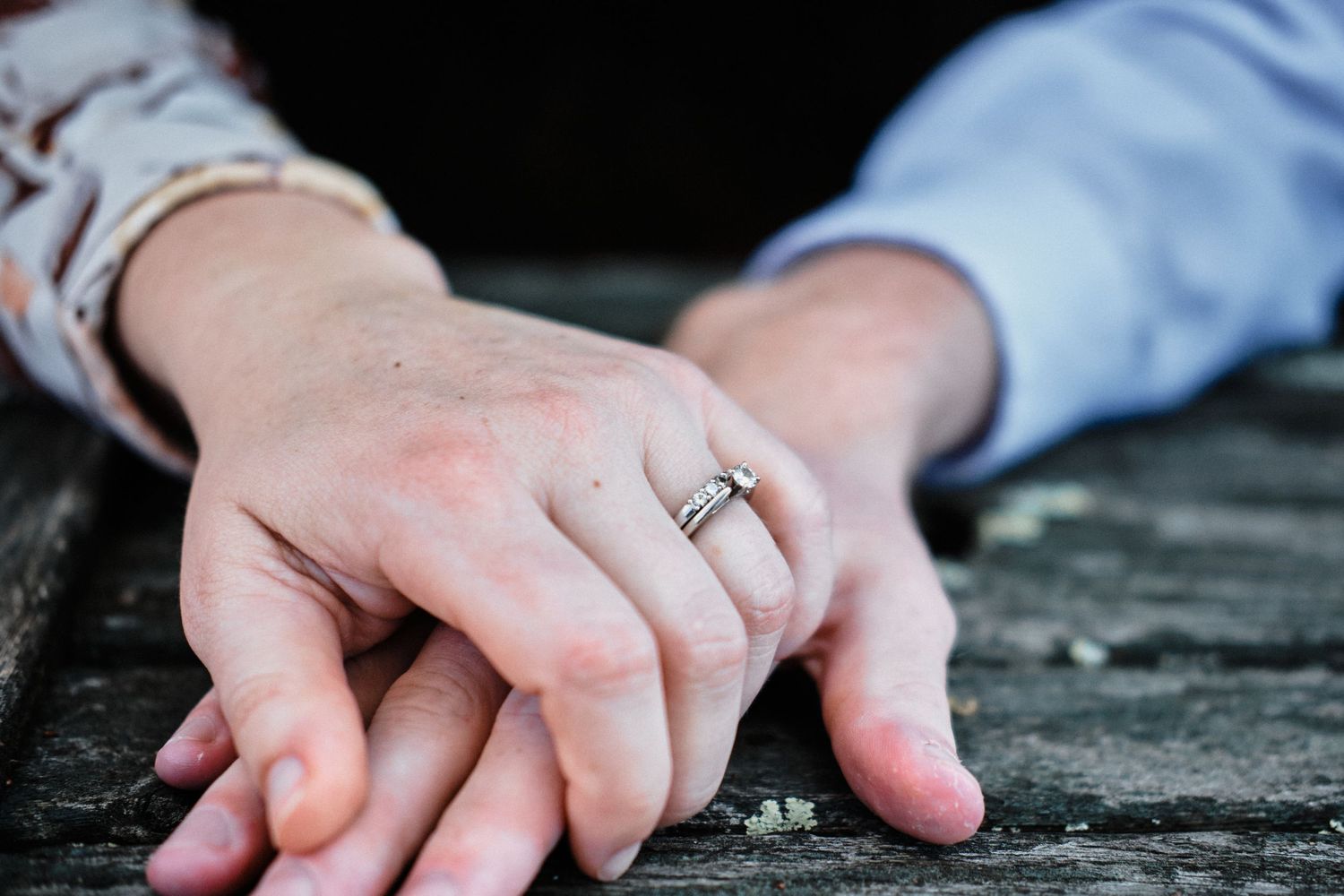 Close-up of hands with engagement ring resting on weathered wooden surface.