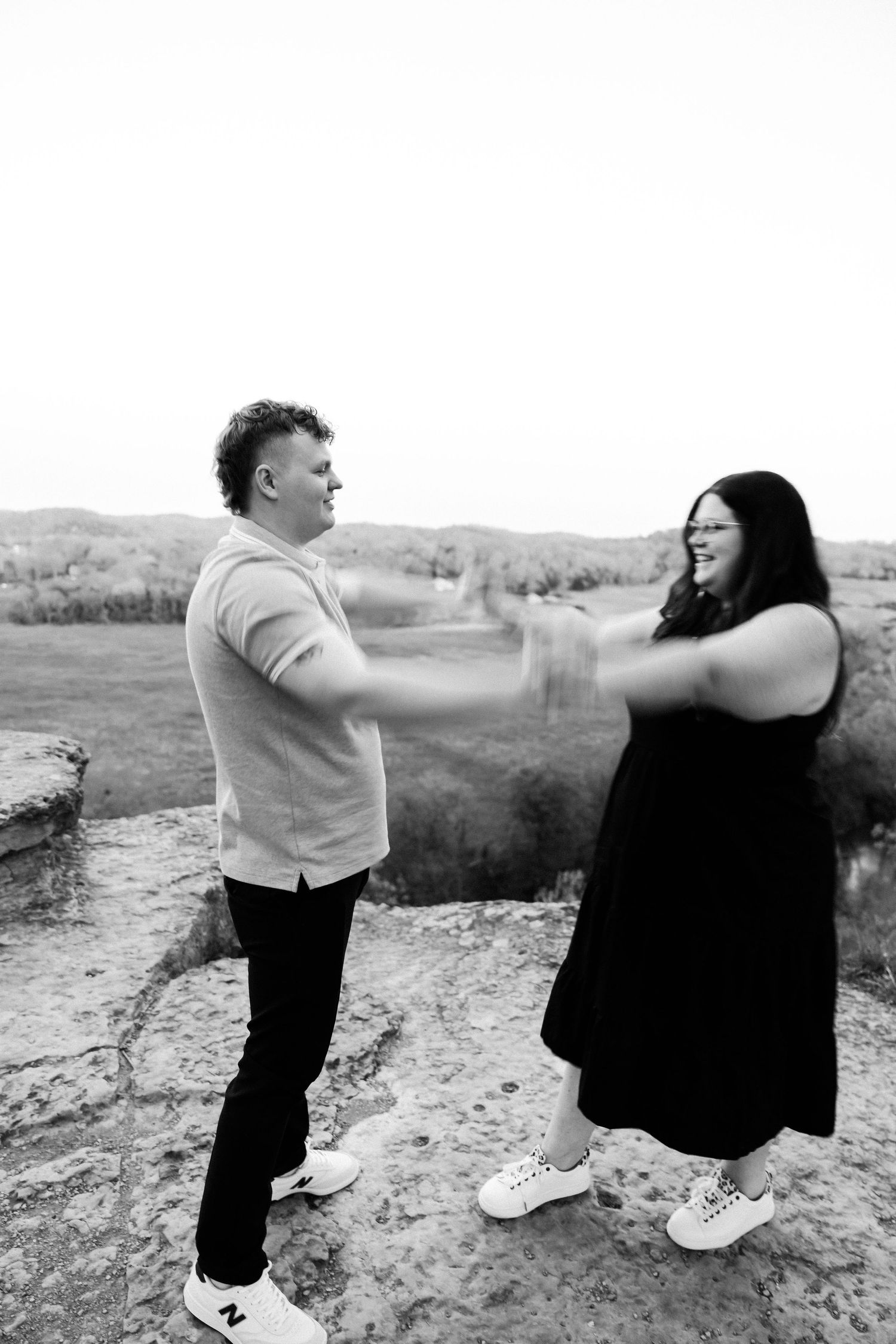 Two people laughing and sharing playful moment on cliff edge with scenic valley view.