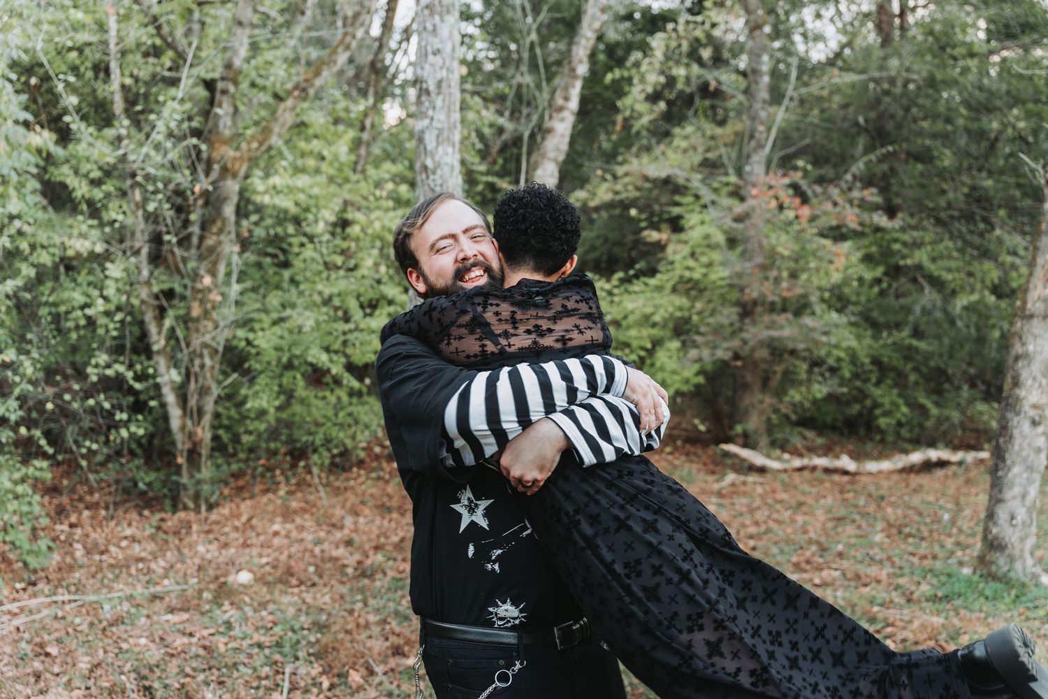 Two people sharing an emotional embrace outdoors among trees in a forest setting.