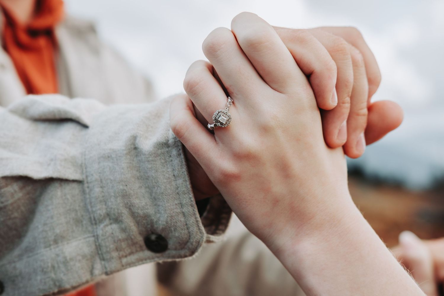 Close-up photo of hands clasped together with an engagement ring, showing a tender moment between a couple.