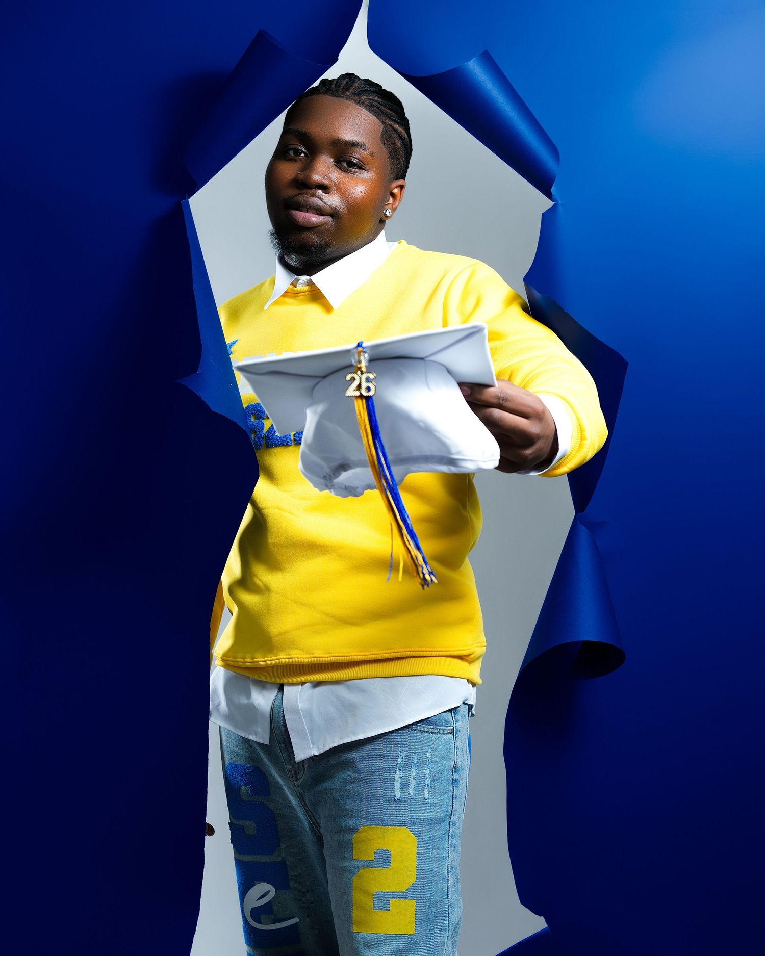 A person in a yellow sweater and jeans poses expressively against a blue background in a photo series.