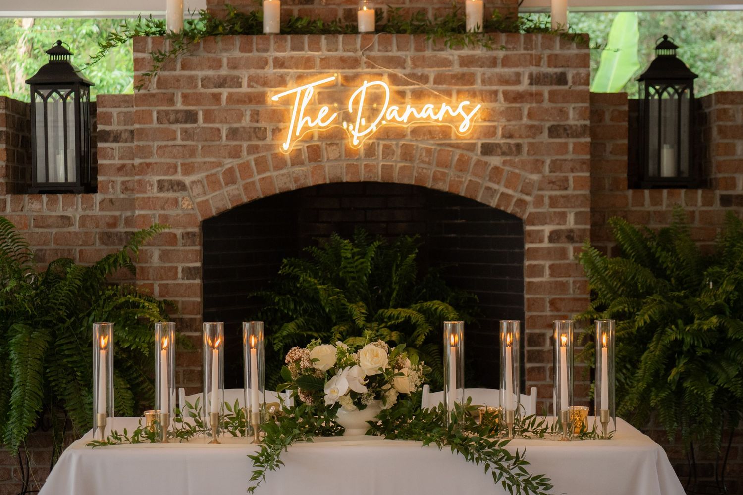 Wedding reception decor features neon 'The Dancing' sign above table with candles and greenery.