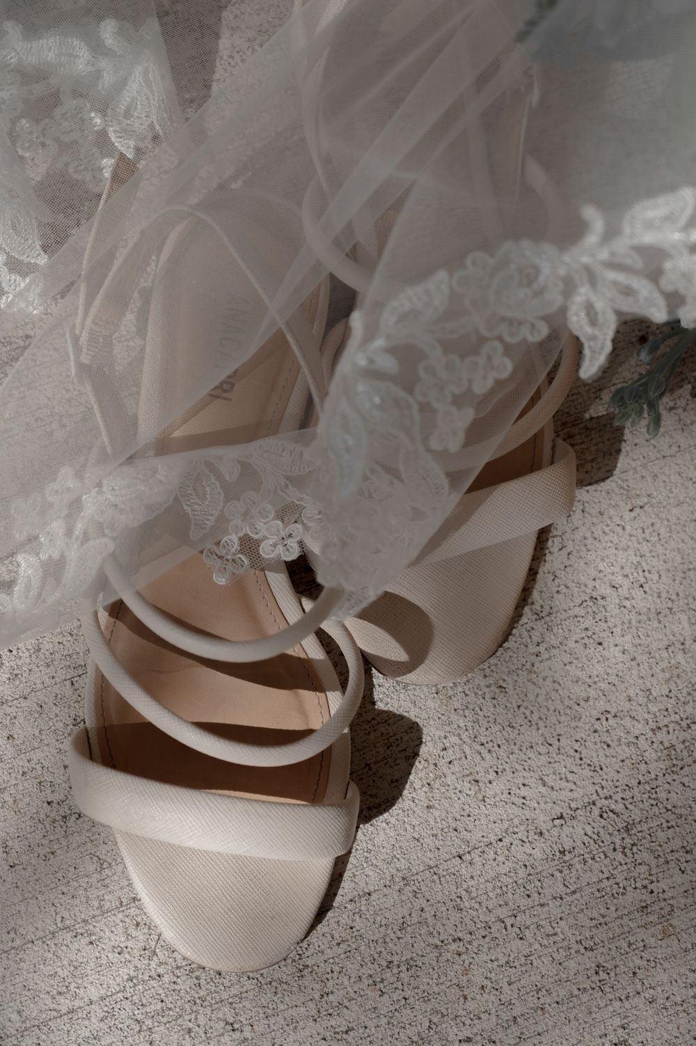 White bridal shoes peeking beneath layers of lace wedding dress hem.