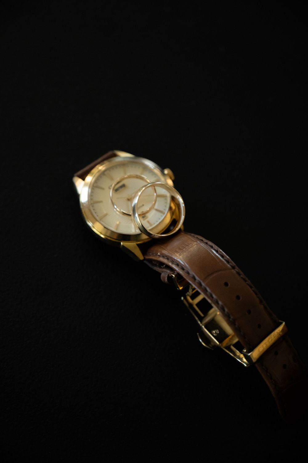 Gold watch with brown leather strap displayed against black background.