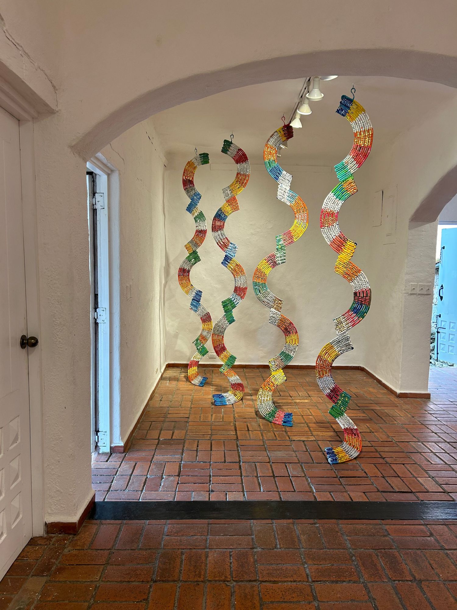 Serpentine plastic chain installation with multicolored segments hanging in white archway.
