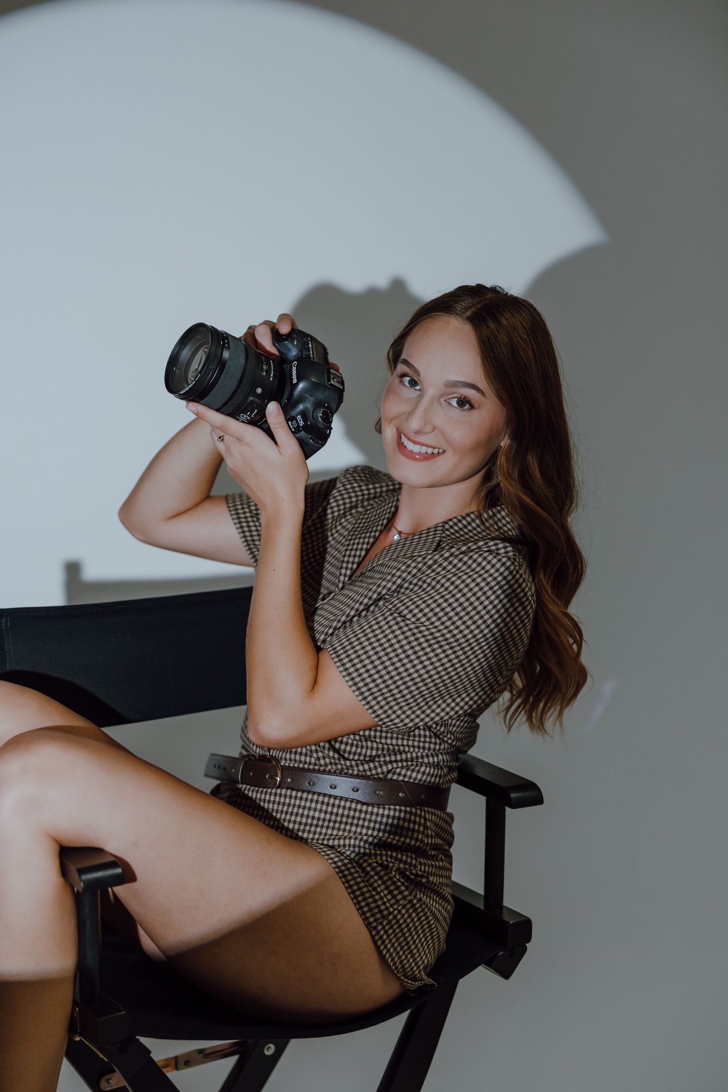 Photographer in white top and jeans holding camera against geometric tiled wall.