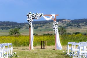 White wedding chairs and archway set up for outdoor ceremony in scenic mountain meadow with blue sky.