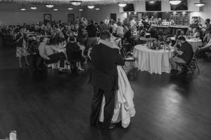 Black and white photo of couples dancing at an elegant reception with tables and chairs arranged throughout the venue.