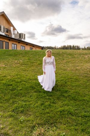 A dreamy wedding scene on a grassy hillside with a white dress flowing in the wind against a cloudy sky backdrop.