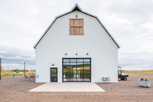 A modern white barn-style building with black accents and large windows against a cloudy sky.