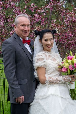 Wedding couple smiling together outdoors with blooming pink flowers in the background.