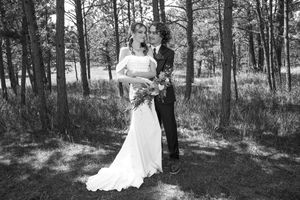 A newlywed couple walks together through a serene wooded area in black and white photography.