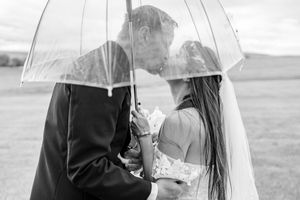 A couple shares an intimate moment under a clear umbrella in a dreamy black and white outdoor setting.