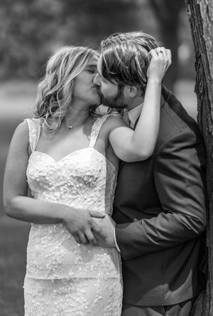 A tender black and white wedding moment captured outdoors as a couple shares an intimate kiss.