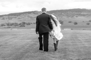 A couple walks together across a scenic hillside meadow with mountains in the distance in black and white.