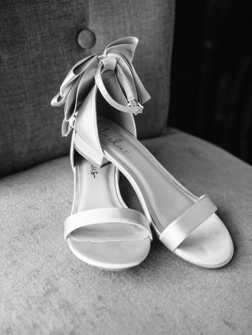 Elegant white bridal sandals with ankle straps displayed on grey fabric.