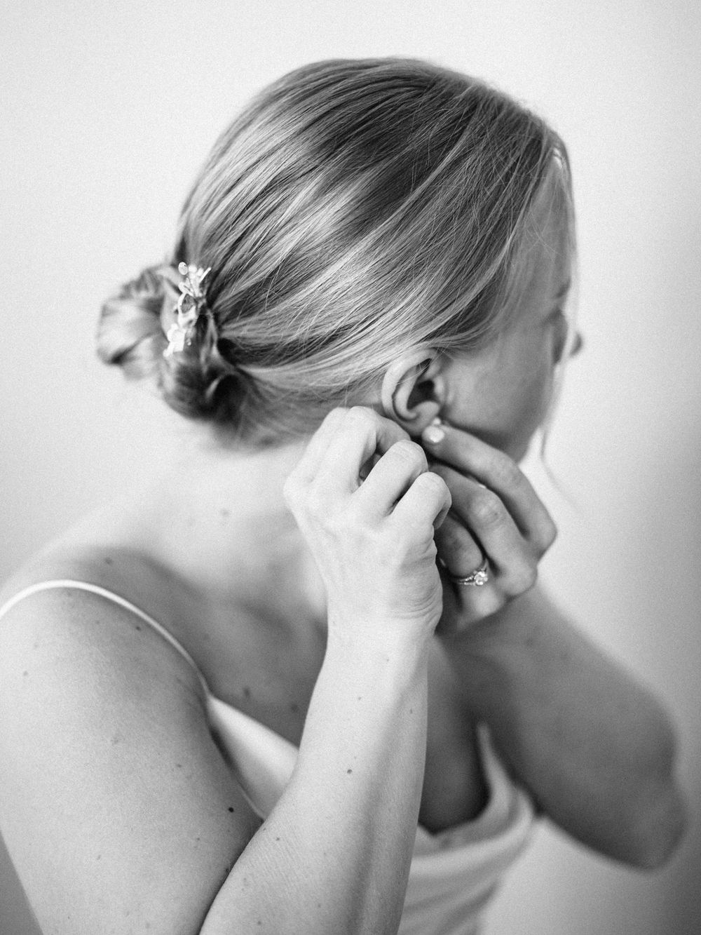 A black and white close-up shot of a bride putting on earrings during wedding preparations.