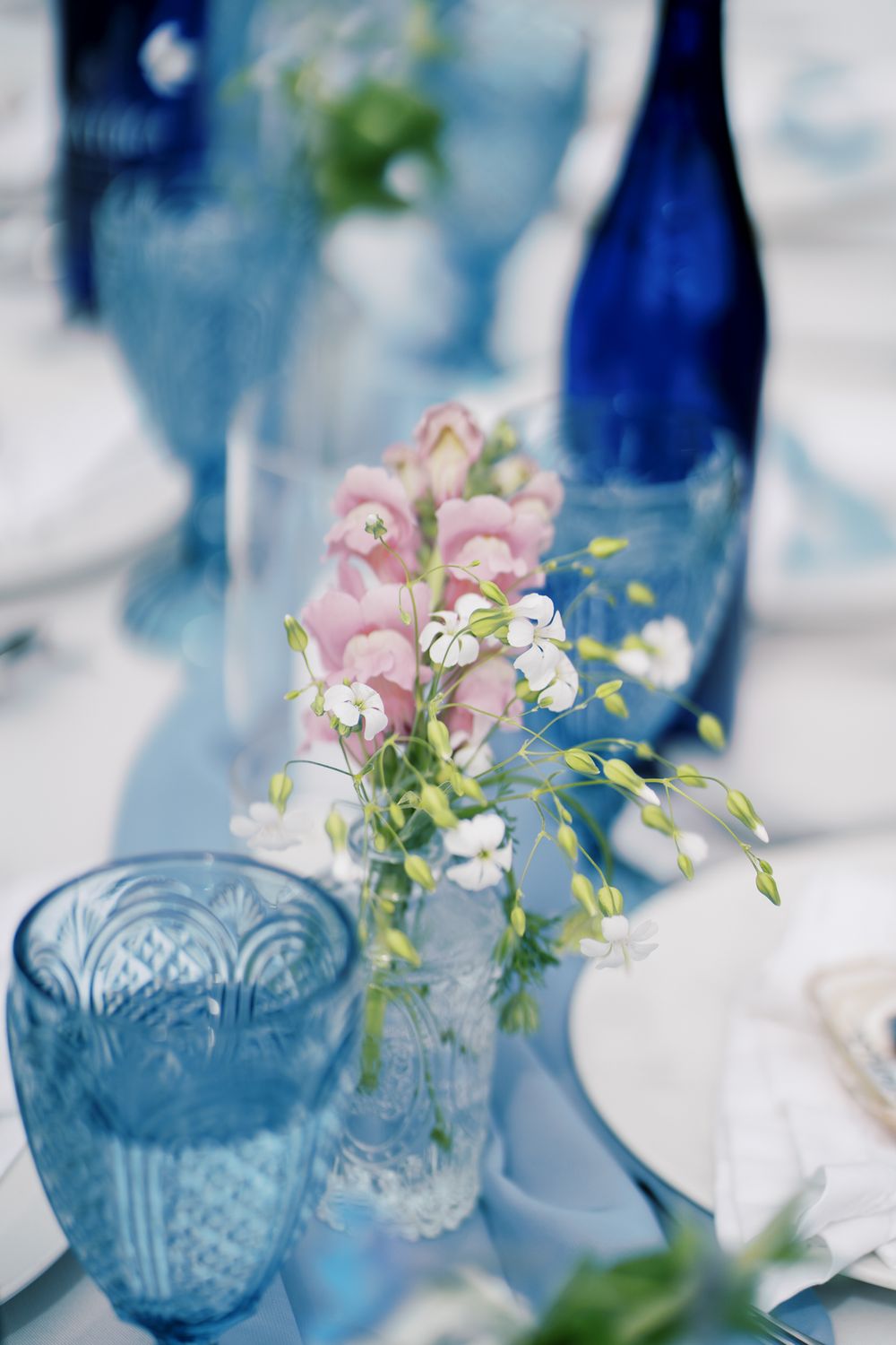 Elegant wedding table setting with blue glass bottles and pink floral arrangements.