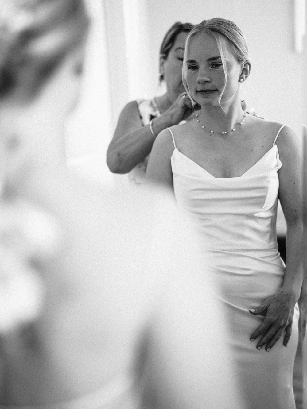 Black and white portrait of bride getting ready in classic white slip dress.