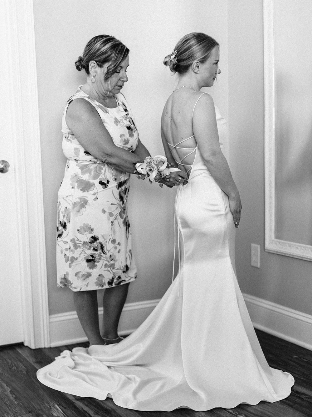 A woman helps adjust a bride's elegant white wedding dress with a flowing train.