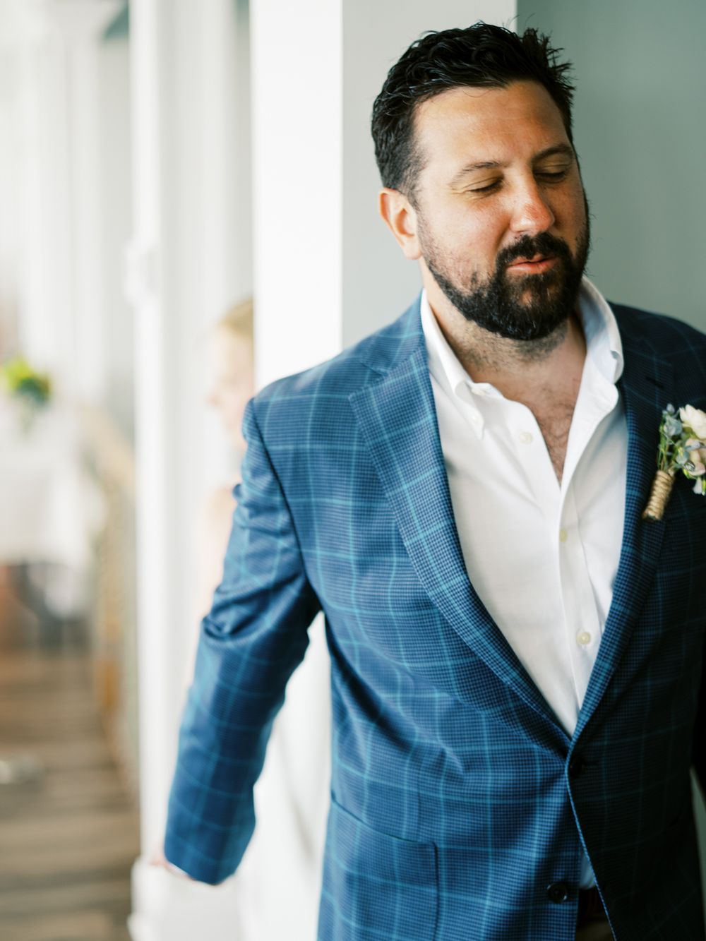 Groom wearing blue plaid blazer and white shirt with boutonniere at wedding.