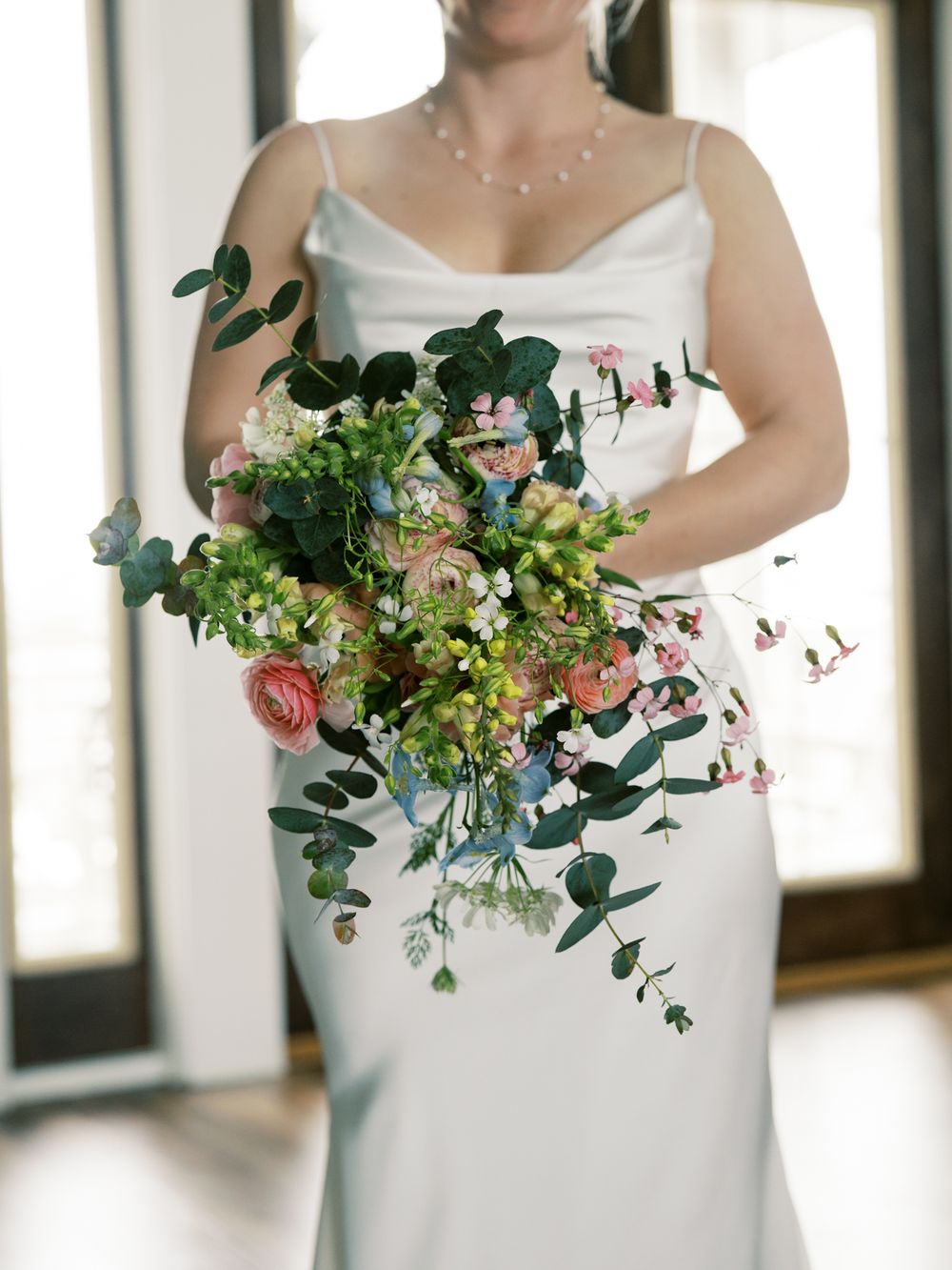 Elegant bridal bouquet with eucalyptus, roses and greenery against white dress.
