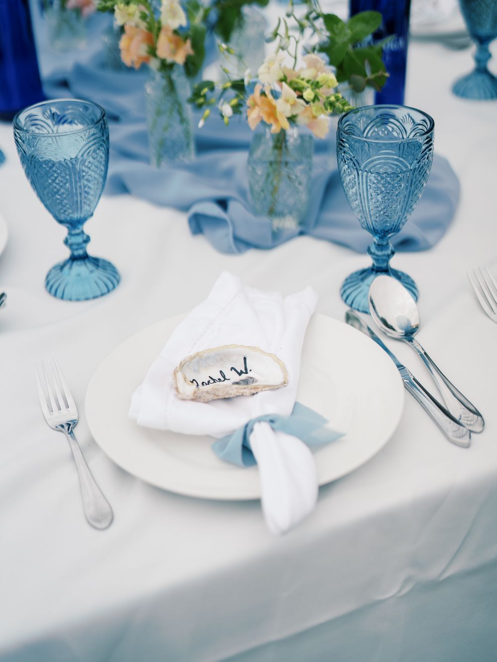 Elegant table setting with vintage blue glassware, white plates, and delicate floral centerpiece.